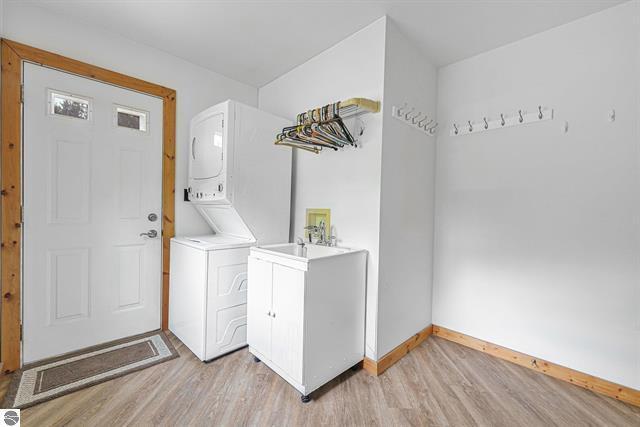 2460 E 26th Rd, Cadillac, MI 49601 - washroom featuring stacked washing machine and dryer, light wood-style flooring, baseboards, and cabinet space