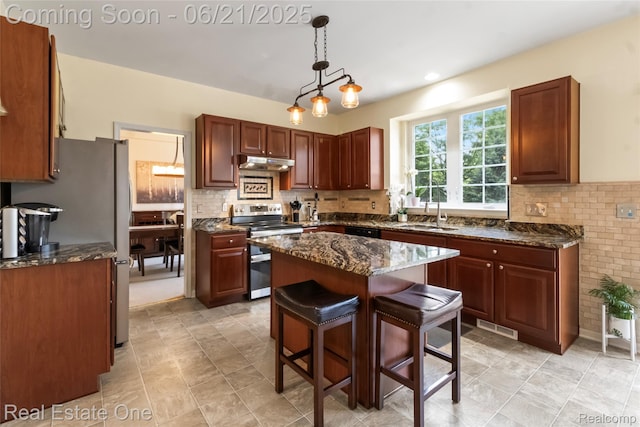 7244 Millrock Ave, Shelby Twp, MI 48317 - kitchen featuring appliances with stainless steel finishes, under cabinet range hood, dark stone counters, pendant lighting, and a kitchen breakfast bar