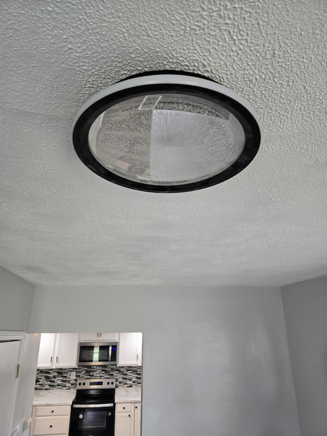 1420 Sweet St, Saginaw, MI 48602 - kitchen view of range with electric stovetop, stainless steel microwave, light countertops, white cabinets, and a textured ceiling