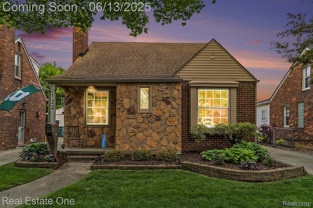 122 N Wilson Ave, Royal Oak, MI 48067 - tudor home featuring a chimney, a shingled roof, a yard, stone siding, and covered porch