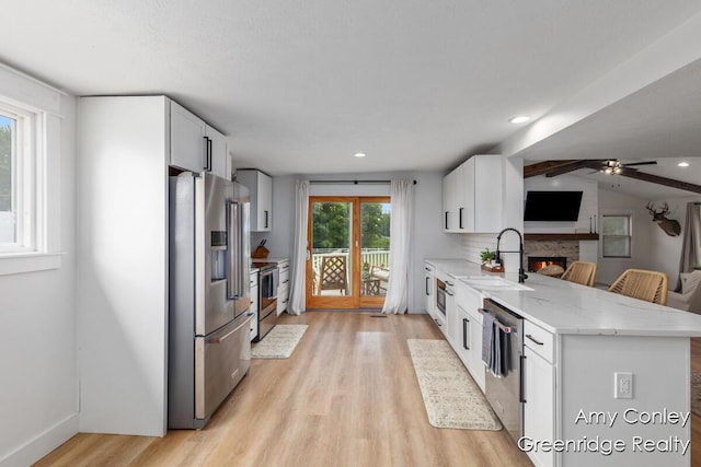 821 W Baseline Rd, Plainwell, MI 49080 - kitchen featuring appliances with stainless steel finishes, a peninsula, light wood-style floors, a warm lit fireplace, and light stone counters