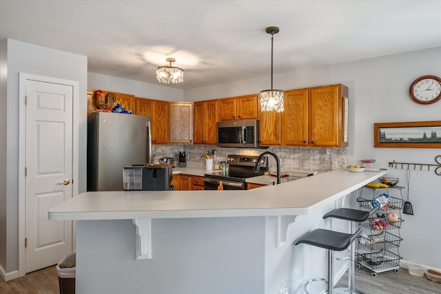 340 E 4th St, Onsted, MI 49265 - kitchen with appliances with stainless steel finishes, brown cabinetry, a peninsula, light countertops, and a kitchen breakfast bar