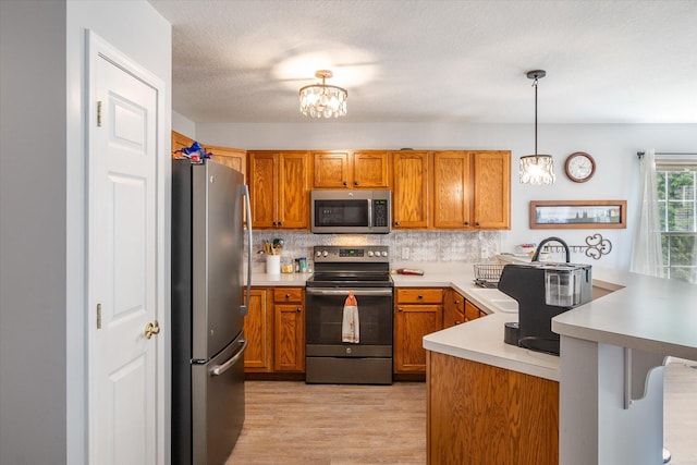 340 E 4th St, Onsted, MI 49265 - kitchen featuring appliances with stainless steel finishes, a peninsula, brown cabinetry, light wood-style flooring, and light countertops