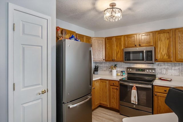 340 E 4th St, Onsted, MI 49265 - kitchen with appliances with stainless steel finishes, brown cabinets, light countertops, tasteful backsplash, and light wood-type flooring