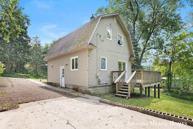 443 Nicholson St, Ionia, MI 48846 - view of home's exterior featuring a gambrel roof, a wooden deck, a chimney, a lawn, and a shingled roof