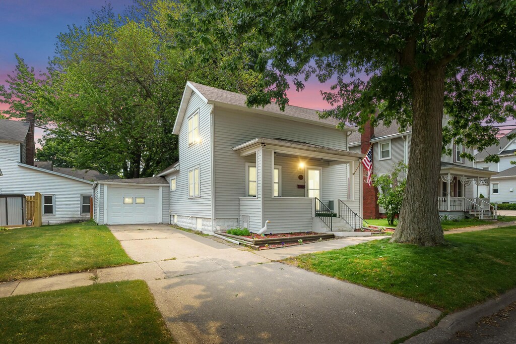 716 Price St, Saint Joseph, MI 49085 - view of front of house with driveway, covered porch, a yard, an outbuilding, and roof with shingles