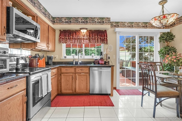 54286 Bradshaw Dr, New Baltimore, MI 48047 - kitchen featuring appliances with stainless steel finishes, dark countertops, light tile patterned flooring, brown cabinets, and hanging light fixtures