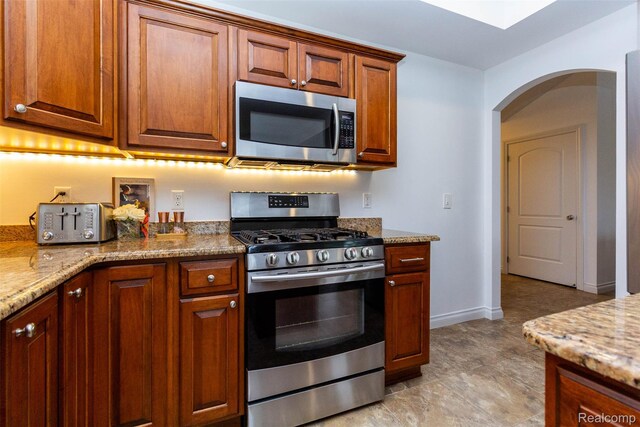 52854 Schafers Run Ct, New Baltimore, MI 48051 - kitchen featuring stainless steel appliances, arched walkways, light stone countertops, and brown cabinetry