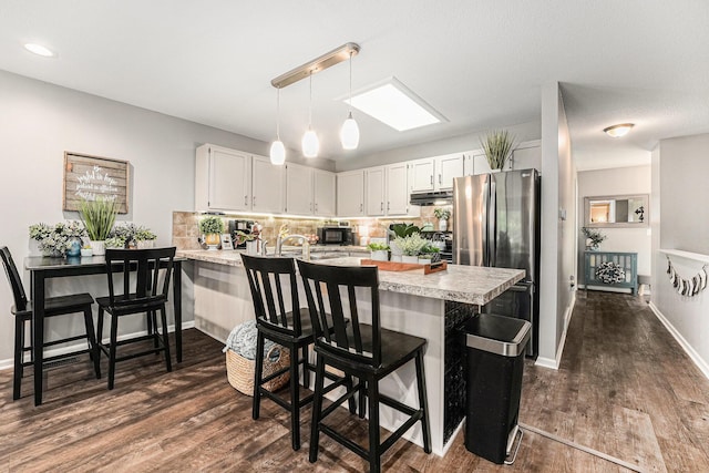 541 Maryland Ave NE Unit 39, Grand Rapids, MI 49503 - kitchen featuring freestanding refrigerator, a peninsula, light countertops, under cabinet range hood, and dark wood-type flooring
