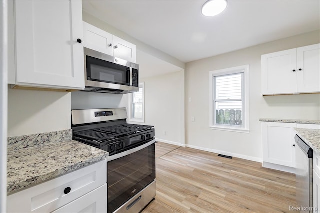 3820 17th St, Grosse Ile, MI 48192 - kitchen featuring appliances with stainless steel finishes, white cabinets, light wood-style floors, and light stone counters