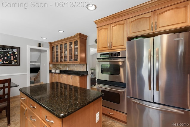 24960 S Cromwell Dr, Franklin, MI 48025 - kitchen featuring appliances with stainless steel finishes, dark stone counters, glass insert cabinets, tasteful backsplash, and a center island