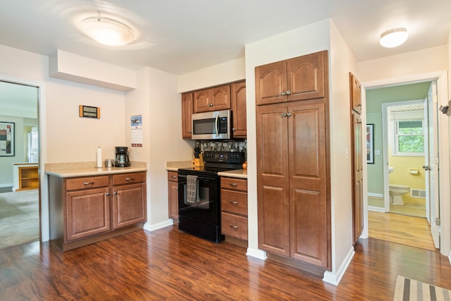 833 S Lansing St, Mason, MI 48854 - kitchen with black range with electric cooktop, stainless steel microwave, dark wood-style floors, light countertops, and brown cabinetry