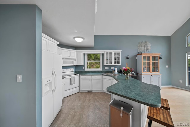 13832 Grandview Dr, Cement City, MI 49233 - kitchen featuring white appliances, a peninsula, a kitchen bar, dark countertops, and white cabinets