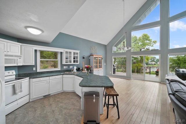 13832 Grandview Dr, Cement City, MI 49233 - kitchen with white appliances, high vaulted ceiling, a peninsula, white cabinetry, and dark countertops