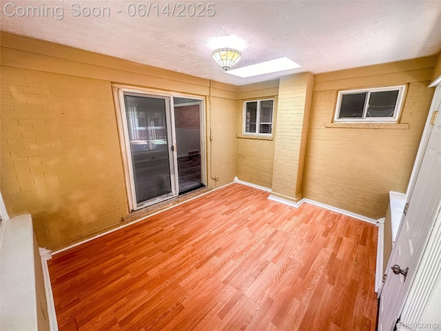 30320 Moulin Ave, Warren, MI 48088 - empty room featuring light wood-type flooring, brick wall, a textured ceiling, and a skylight