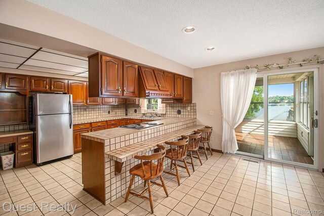 14050 Shannon Dr, Cement City, MI 49233 - kitchen with freestanding refrigerator, a peninsula, light tile patterned floors, tasteful backsplash, and a kitchen bar