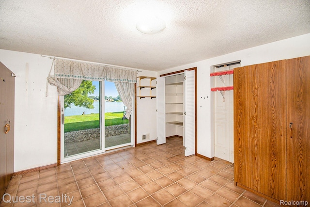 14050 Shannon Dr, Cement City, MI 49233 - unfurnished bedroom featuring a textured ceiling, two closets, a water view, and tile patterned flooring