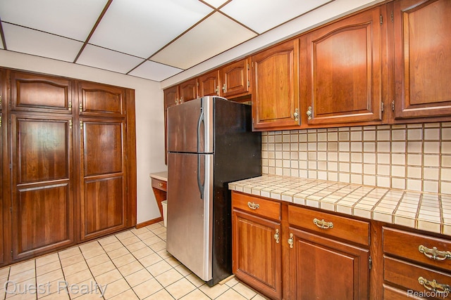 14050 Shannon Dr, Cement City, MI 49233 - kitchen featuring freestanding refrigerator, tasteful backsplash, tile countertops, light tile patterned floors, and brown cabinets