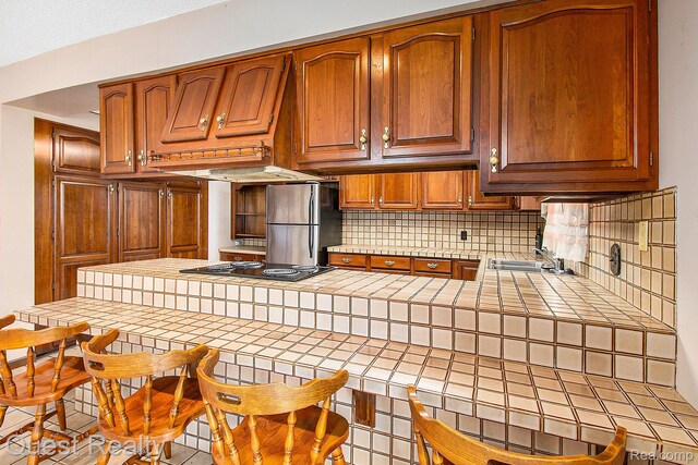 14050 Shannon Dr, Cement City, MI 49233 - kitchen with tile counters, freestanding refrigerator, decorative backsplash, a peninsula, and brown cabinetry