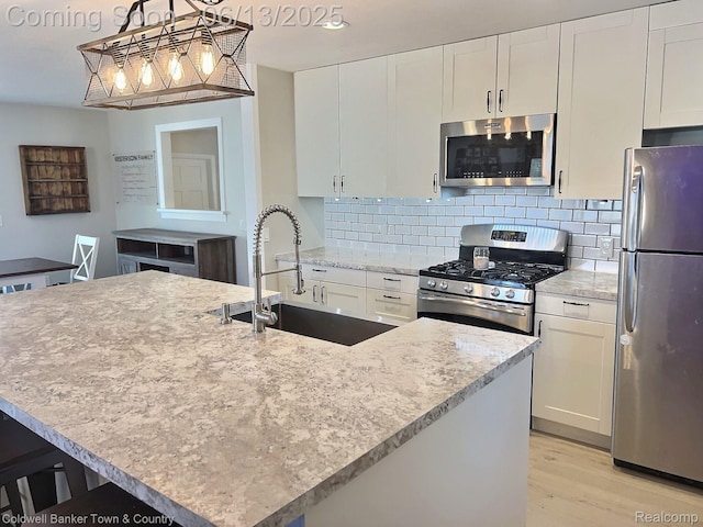 8811 Coyle Dr, Pinckney, MI 48169 - kitchen featuring stainless steel appliances, light wood finished floors, white cabinets, backsplash, and decorative light fixtures