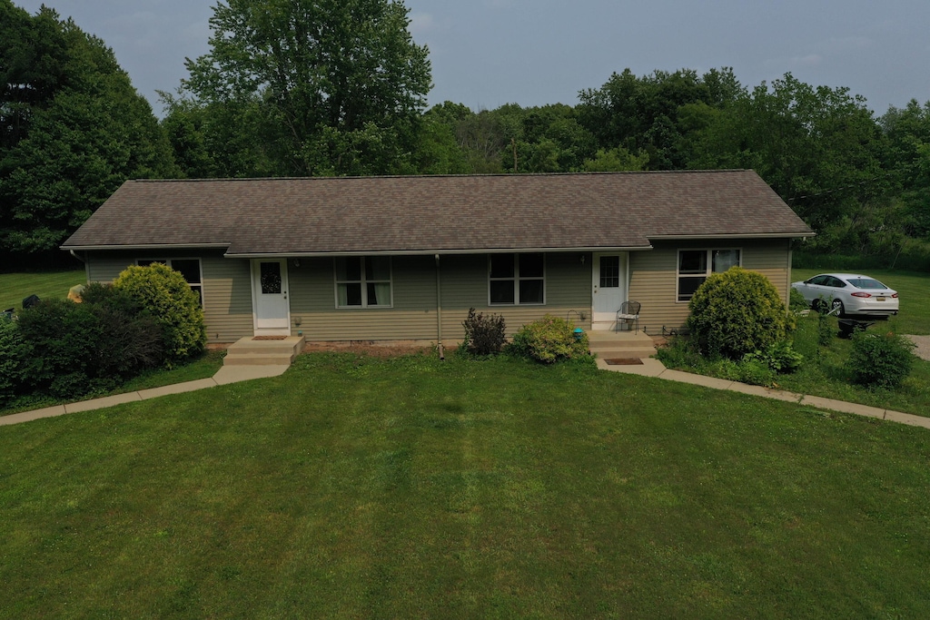 single story home featuring a front lawn, roof with shingles, and a view of trees