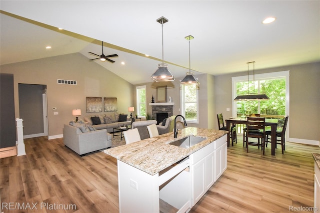 74 Candlelight, Brighton, MI 48114 - kitchen featuring white cabinets, a stone fireplace, light wood finished floors, a center island with sink, and pendant lighting
