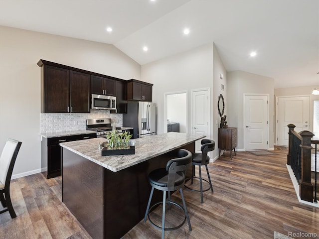 1470 Duncan Dr, Chelsea, MI 48118 - kitchen featuring stainless steel appliances, light stone countertops, dark brown cabinets, a center island, and decorative backsplash