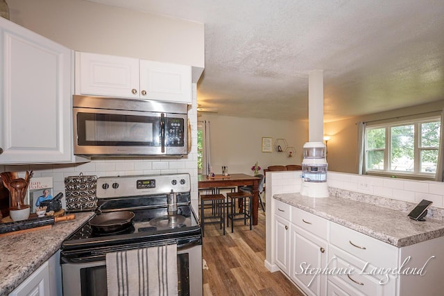 348 Yuba St, Muskegon, MI 49442 - kitchen featuring stainless steel appliances, wood finished floors, white cabinetry, decorative backsplash, and a textured ceiling