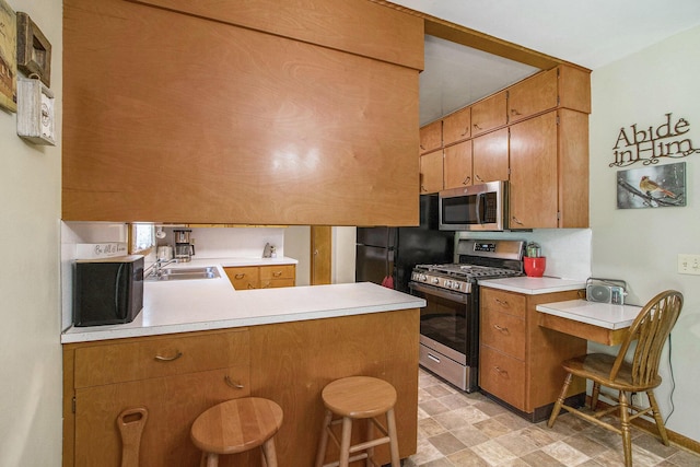 6361 Plainfield Ave, Kalamazoo, MI 49048 - kitchen featuring appliances with stainless steel finishes, a peninsula, light countertops, brown cabinetry, and a breakfast bar area