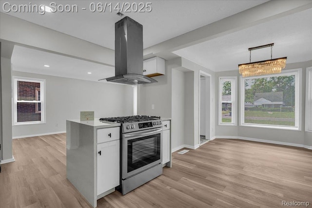 18336 Glastonbury Rd, Detroit, MI 48219 - kitchen with stainless steel gas range, island range hood, white cabinets, light wood-type flooring, and light countertops