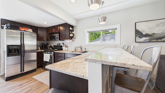 1204 Witham Rd, Muskegon, MI 49445 - kitchen with stainless steel appliances, dark brown cabinets, light wood-style flooring, hanging light fixtures, and light stone countertops
