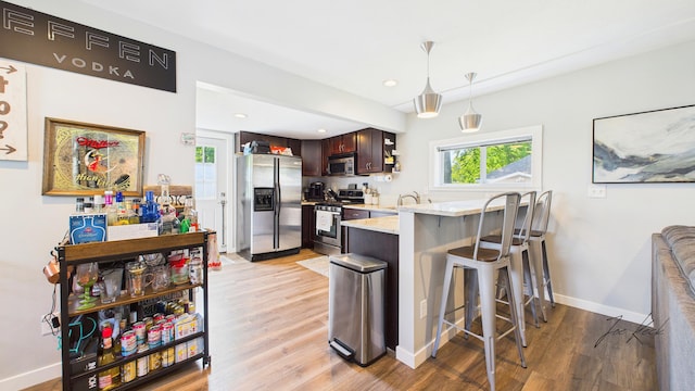 1204 Witham Rd, Muskegon, MI 49445 - kitchen featuring appliances with stainless steel finishes, light wood-style floors, a peninsula, a kitchen breakfast bar, and dark brown cabinetry