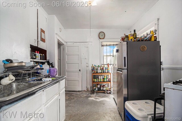 3620 Holborn St, Detroit, MI 48211 - kitchen featuring freestanding refrigerator, unfinished concrete floors, dark countertops, and white cabinets