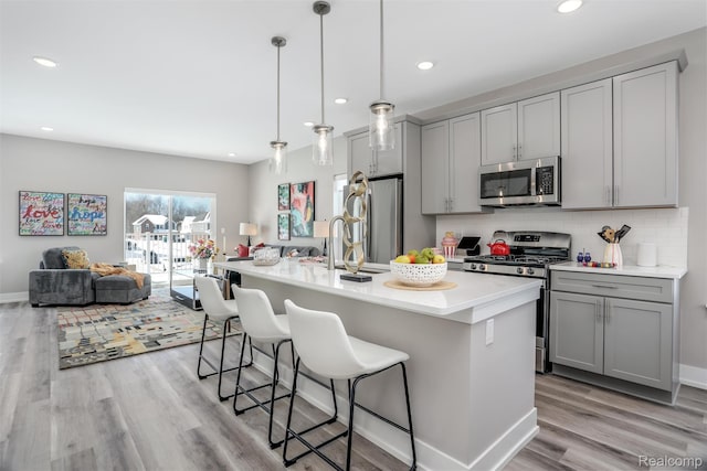 4837 Lismore Ln, Troy, MI 48085 - kitchen featuring appliances with stainless steel finishes, gray cabinets, light wood-type flooring, light countertops, and a breakfast bar area
