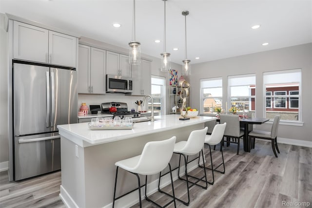4837 Lismore Ln, Troy, MI 48085 - kitchen featuring stainless steel appliances, a kitchen island with sink, light wood-type flooring, light countertops, and a kitchen breakfast bar