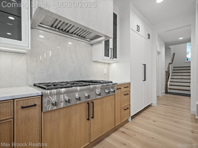 4331 Spruce Hill Ln, Birmingham, MI 48301 - kitchen with custom exhaust hood, stainless steel gas cooktop, light wood-style flooring, decorative backsplash, and glass insert cabinets