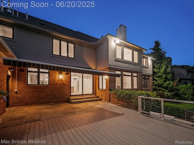 4331 Spruce Hill Ln, Birmingham, MI 48301 - back of house at night featuring entry steps, stucco siding, a chimney, a deck, and brick siding