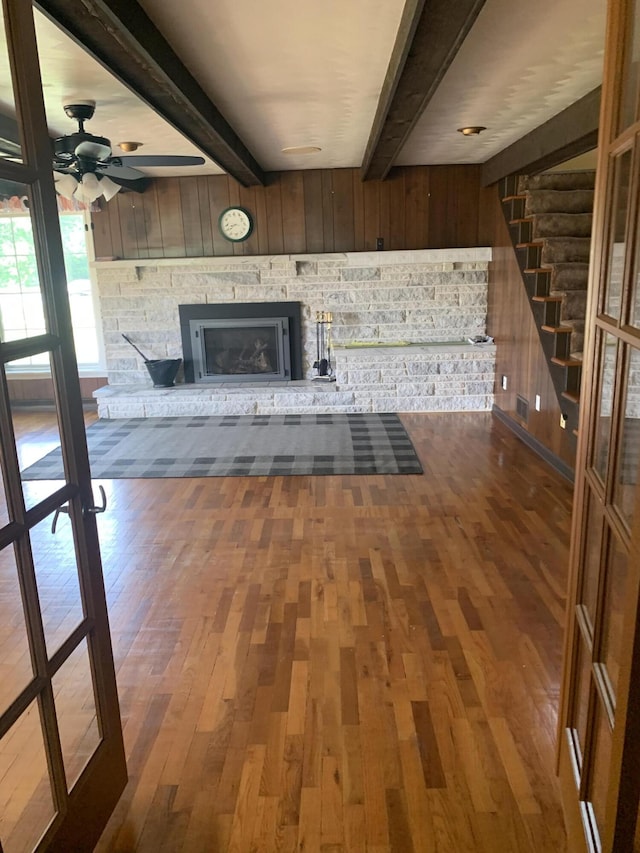 5513 S Waverly Rd, Lansing, MI 48911 - unfurnished living room with beamed ceiling, wood finished floors, wooden walls, a stone fireplace, and ceiling fan