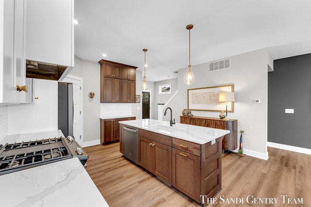 806 S Lake St, Whitehall, MI 49461 - kitchen with stainless steel dishwasher, light wood-type flooring, light stone counters, hanging light fixtures, and a center island with sink