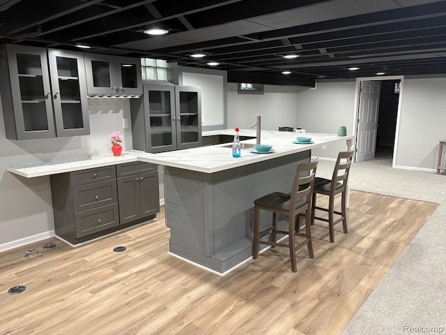 2211 Parkside St, Trenton, MI 48183 - kitchen with gray cabinetry, glass insert cabinets, a kitchen bar, an island with sink, and light wood-style floors
