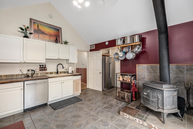 626 Hiscock St, Ann Arbor, MI 48103 - kitchen featuring stainless steel appliances, a wood stove, high vaulted ceiling, white cabinets, and dark countertops