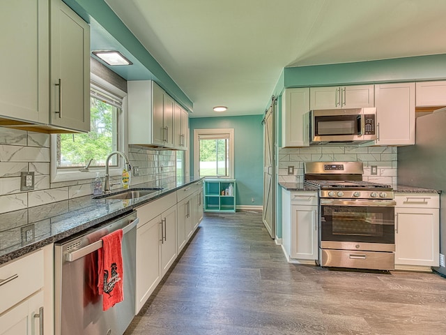 219 Park St, Tecumseh, MI 49286 - kitchen featuring appliances with stainless steel finishes, decorative backsplash, dark stone counters, light wood-type flooring, and white cabinetry