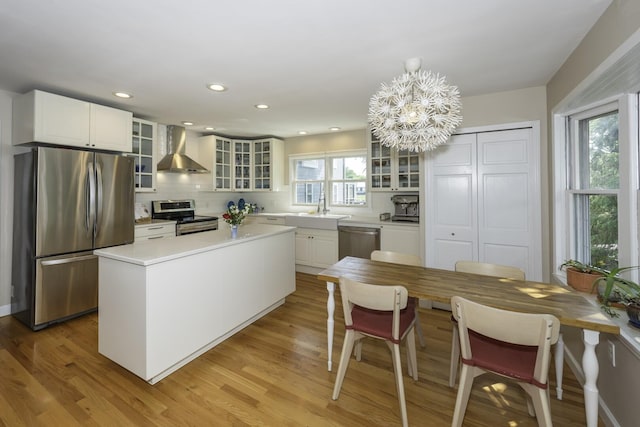 3444 Broad St, Dexter, MI 48130 - kitchen featuring stainless steel appliances, wall chimney range hood, a chandelier, light wood-style floors, and glass insert cabinets