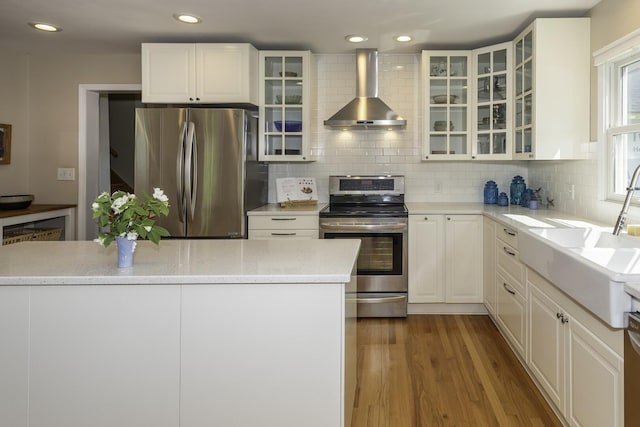 3444 Broad St, Dexter, MI 48130 - kitchen with appliances with stainless steel finishes, wall chimney range hood, light wood-style flooring, tasteful backsplash, and white cabinets