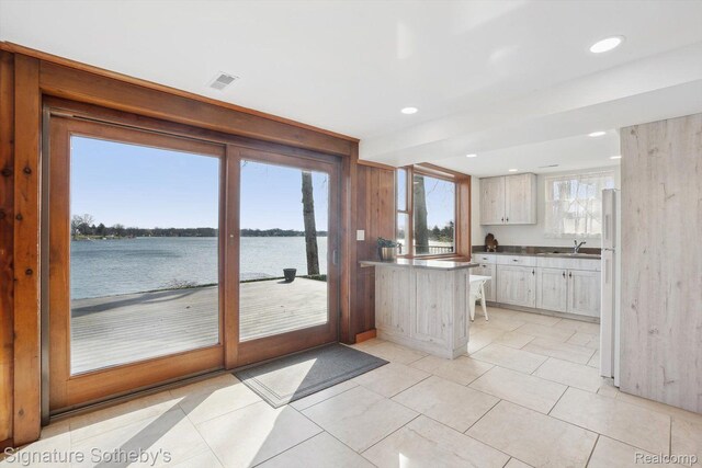 3806 Island Park Dr, Waterford, MI 48329 - kitchen with a peninsula, a water view, light tile patterned floors, recessed lighting, and white cabinetry