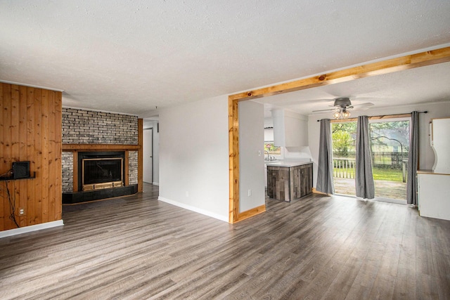 51591 Oak Dr, Mattawan, MI 49071 - unfurnished living room with a textured ceiling, wood finished floors, a brick fireplace, ceiling fan, and wood walls