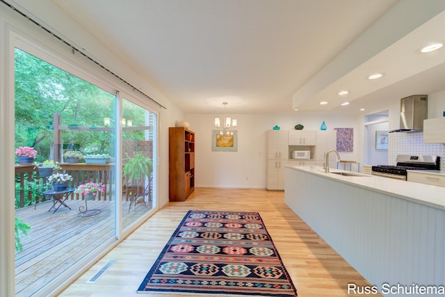 1366 W Norton Ave, Muskegon, MI 49441 - kitchen with wall chimney range hood, gas stove, white microwave, a chandelier, and light wood-style flooring