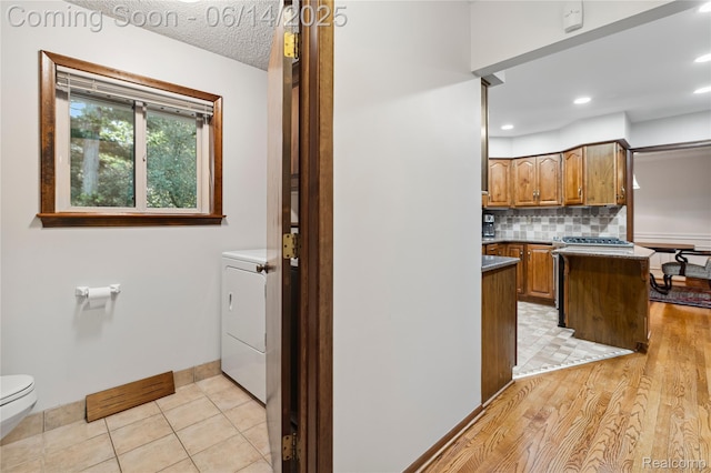 5614 Warbler Dr, Clarkston, MI 48346 - kitchen featuring tasteful backsplash, washer / clothes dryer, brown cabinets, a peninsula, and recessed lighting