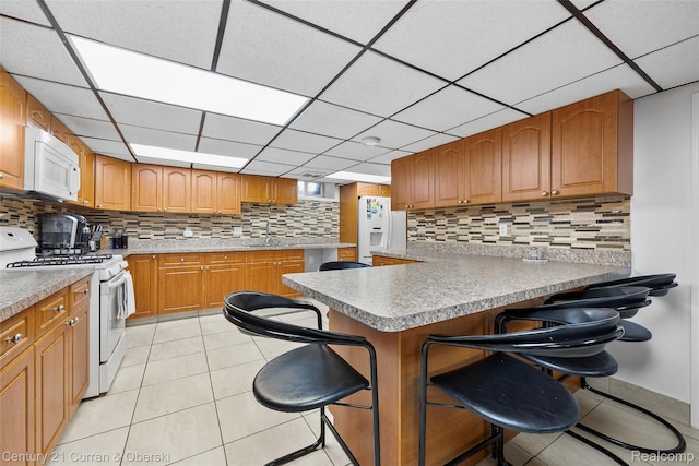7561 Esper Blvd, Dearborn, MI 48126 - kitchen featuring white appliances, a breakfast bar area, backsplash, a paneled ceiling, and light tile patterned flooring