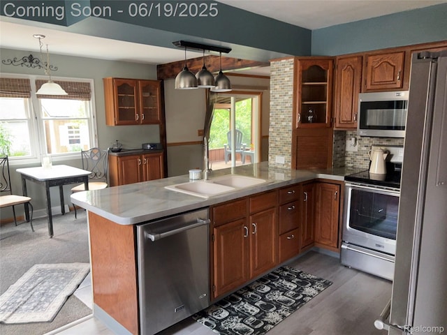 1118 Pine St, Grand Ledge, MI 48837 - kitchen featuring appliances with stainless steel finishes, a peninsula, brown cabinetry, glass insert cabinets, and pendant lighting